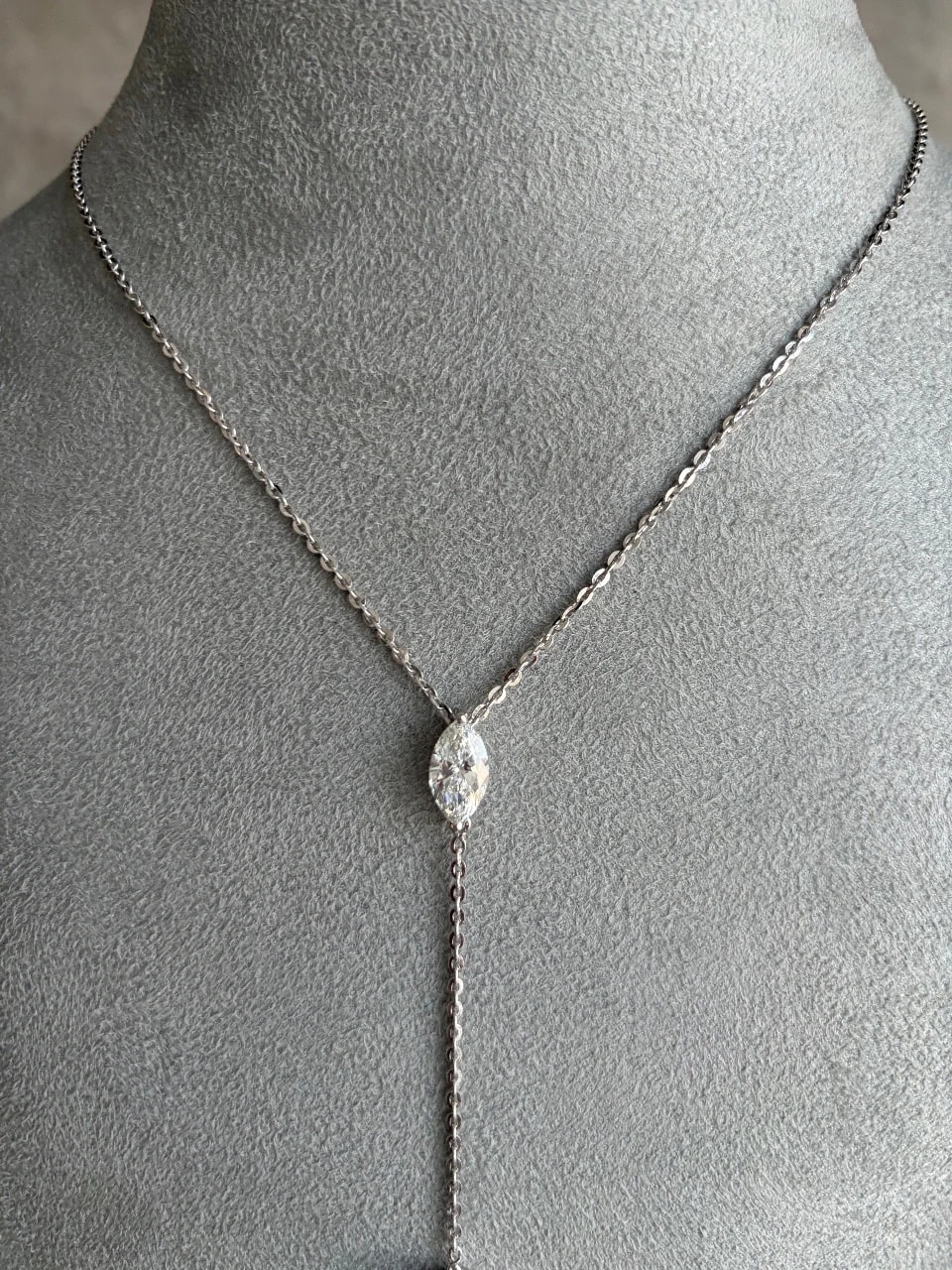 A phone photo of the lariat on a grey velvet display bust: the marquise diamond at the neck, the drop chain running out of frame