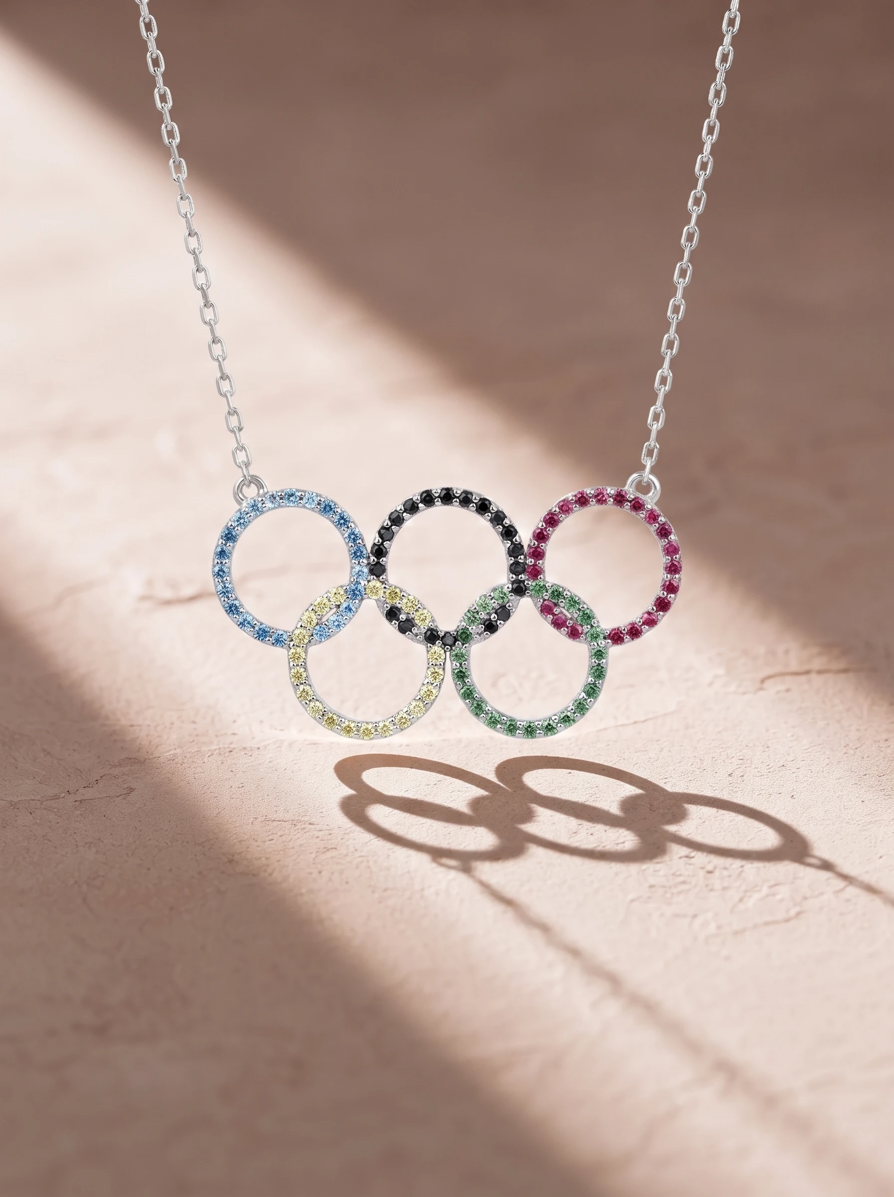 The coloured Olympic pendant on pink stone in a raking shaft of sunlight, its rings casting long shadows