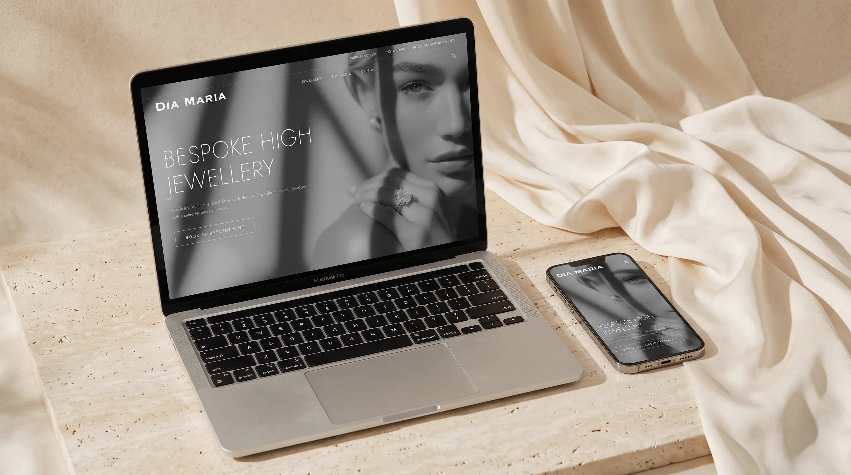 The DiaMaria website on a laptop and a phone, resting on ivory travertine beside a fold of ivory silk